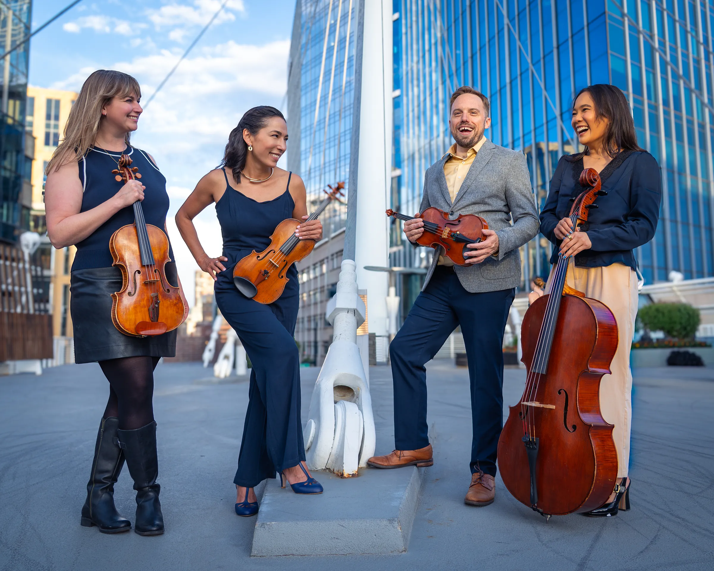 The four members of Midnight Post laughing together in downtown Denver, instruments in hand